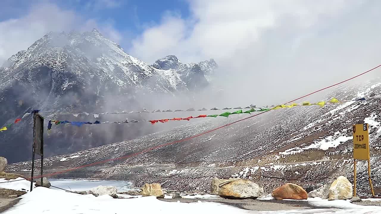 montaña nevada con un cielo dramático a través del marco borroso de las banderas del budismo en el día en que se toma un video en sela pass tawang arunachal pradesh india