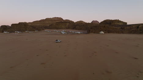 Pickup-Truck-Fährt-Durch-Die-Wüste-Wadi-Rum-Zu-Einem-Campingplatz-Mit-Vielen-Zelten,-Umgeben-Von-Felsformationen-In-Jordanien---Kamerafahrt