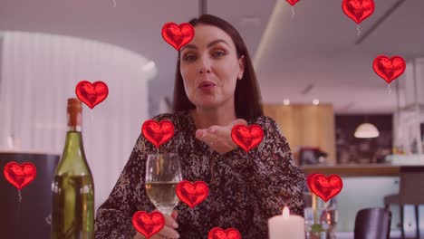 animation of heart icons over happy caucasian woman with wine having video call