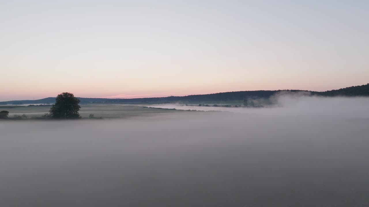Aerial dolly above wispy fog drifting over calm waters at dusk, creating a serene and atmospheric scene