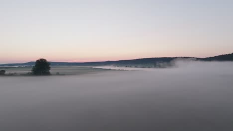 aerial dolly above wispy fog drifting over calm waters at dusk, creating a serene and atmospheric scene