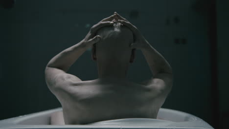 pale bald skinny man takes a bath in the creepy old bathroom at night