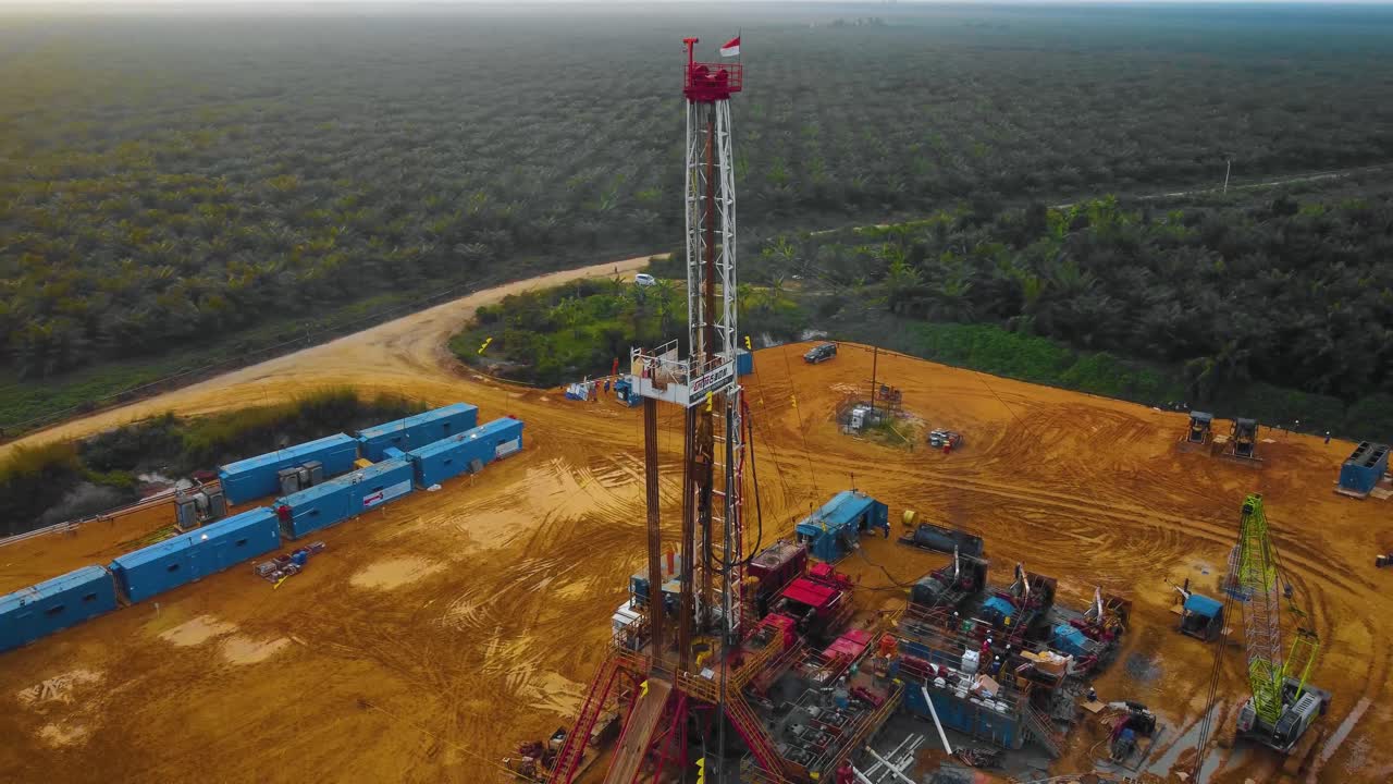 imágenes cinematográficas de drones de la estructura del equipo de la plataforma de perforación en tierra para la exploración y explotación de petróleo en medio de la jungla rodeada de palmeras durante la puesta de sol y el alto precio del petróleo