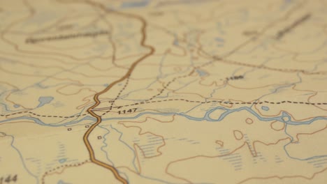 Macro-shot-of-printed-map-following-a-water-course,-contours,-shallow-DOF