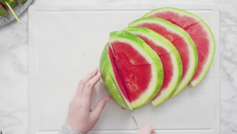 slicing red watermelon into small pieces on a white cutting board.