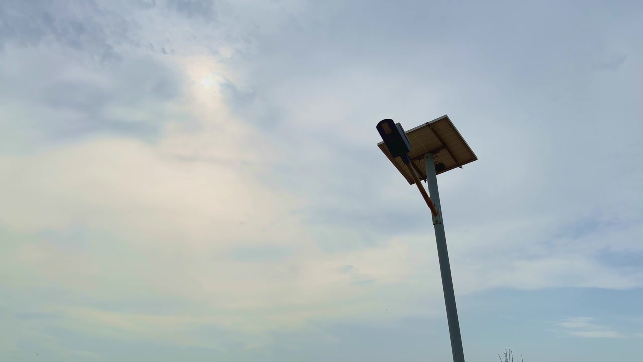 Pemandangan luas menunjukkan lampu jalan bertenaga surya dengan indikator status hijau berkedip yang mengonfirmasi operasi pengisian daya normal di bawah langit berawan dramatis dan lanskap terbuka