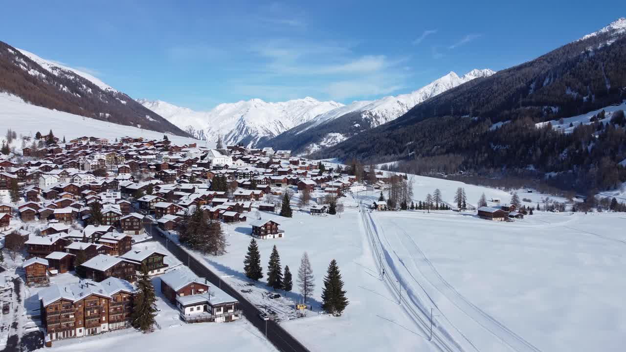 Vistas aéreas con dron de pueblos alpinos cubiertos de nieve en Obergoms, Suiza, con las montañas del paso de Furka dominando el paisaje invernal. Pueblos tradicionales rodeados de nieve alpina profunda.
