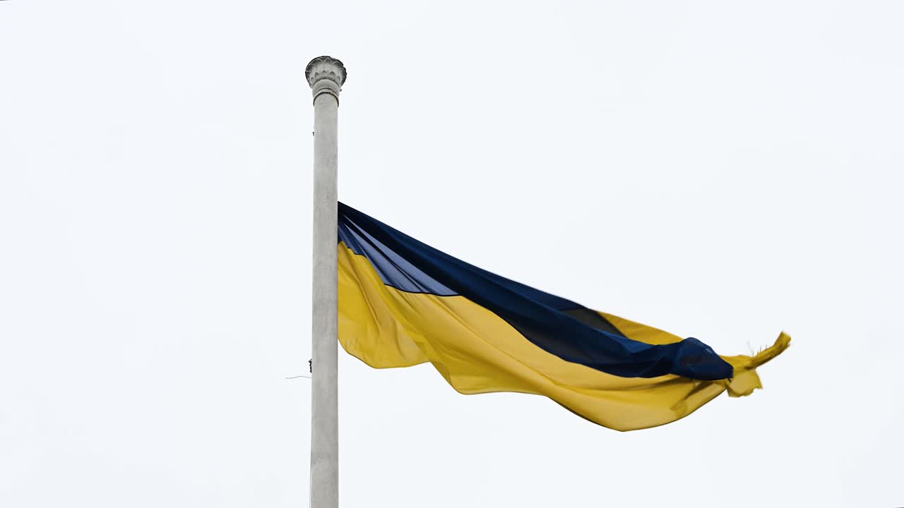 The Ukrainian flag fluttering on a tall post, swaying with the wind on a cloudy, breezy day, highlighting the flag as it moves with the elements.