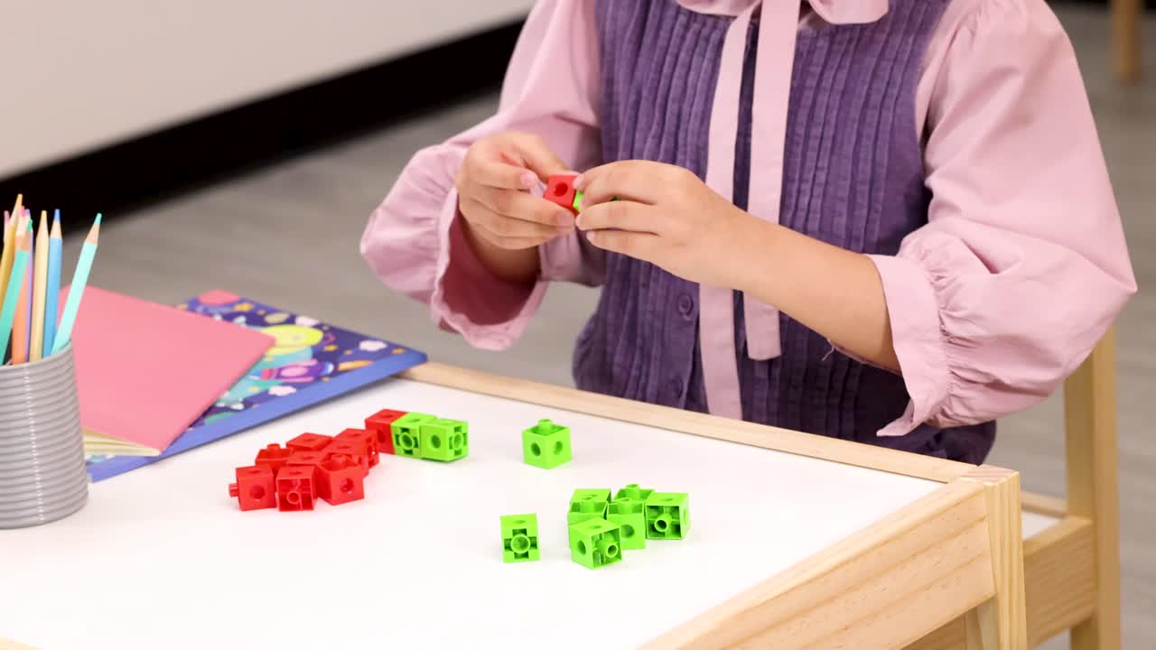 Child’s hands sort red and green plastic cubes on bright classroom table, static shot
