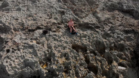 disparo de dron de inversión de un hombre sentado en un acantilado de piedra caliza que revela olas rompiendo en una costa