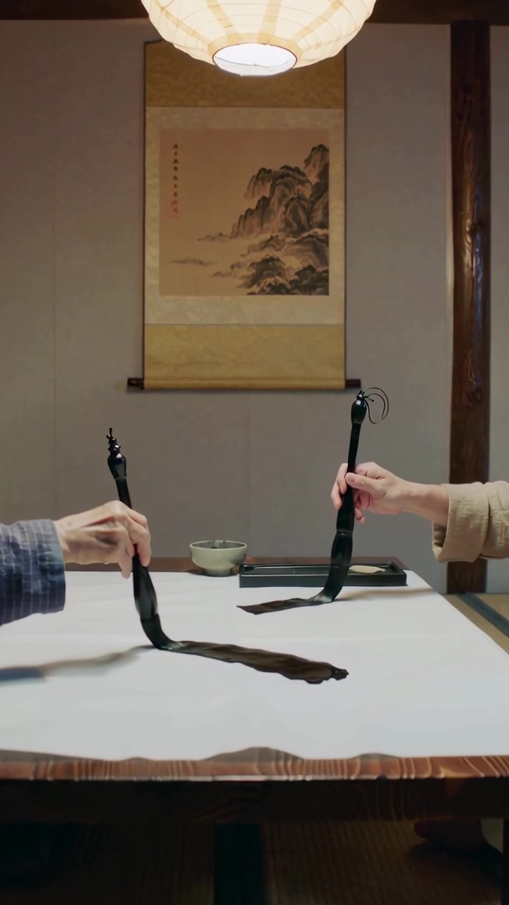 Video verticale: Mentore e studente in kimono che abbassano i pennelli praticando shodo su un foglio in una sala tatami