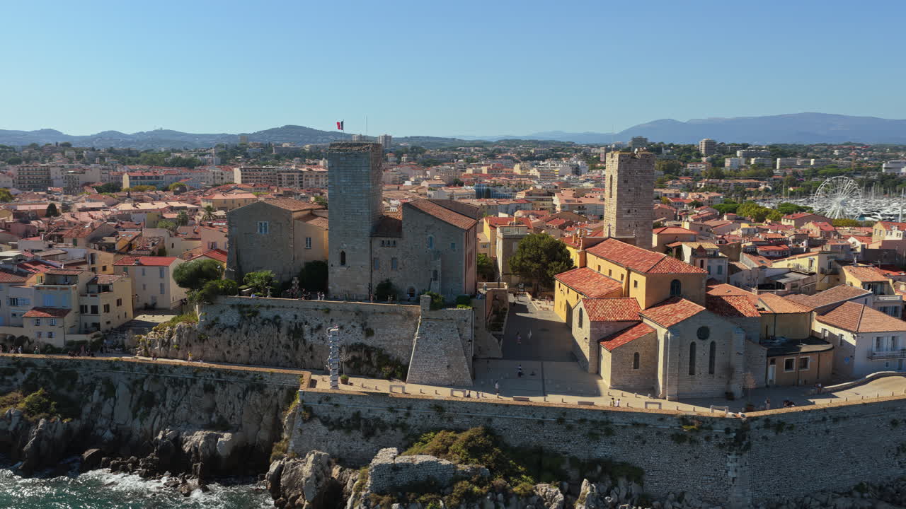 Aerial drone view of the Picasso Museum and medieval stone ramparts overlooking Antibes marina, with yachts docked and the Old Town's terracotta rooftops