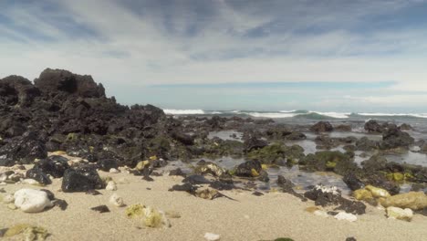 Low-angle-of-large-lava-rock-formation-on-the-beach-with-waves-slowly-and-gently-coming-in