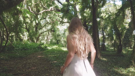 blonde girl walks in tropical forest, turns around and looks into camera