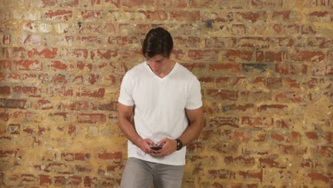 caucasian man using a smartphone on a brick wall