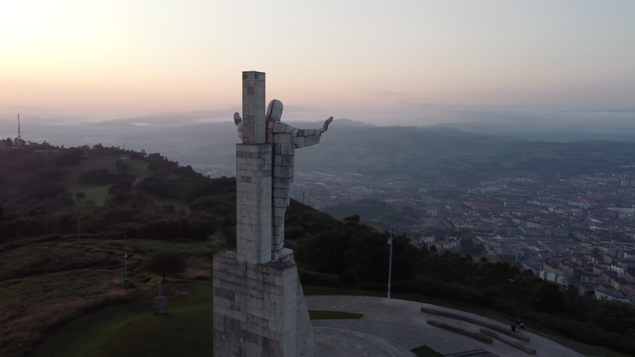 drone orbita alrededor de una gran estatua de hormigón durante el amanecer, revelando la ciudad de oviedo, españa