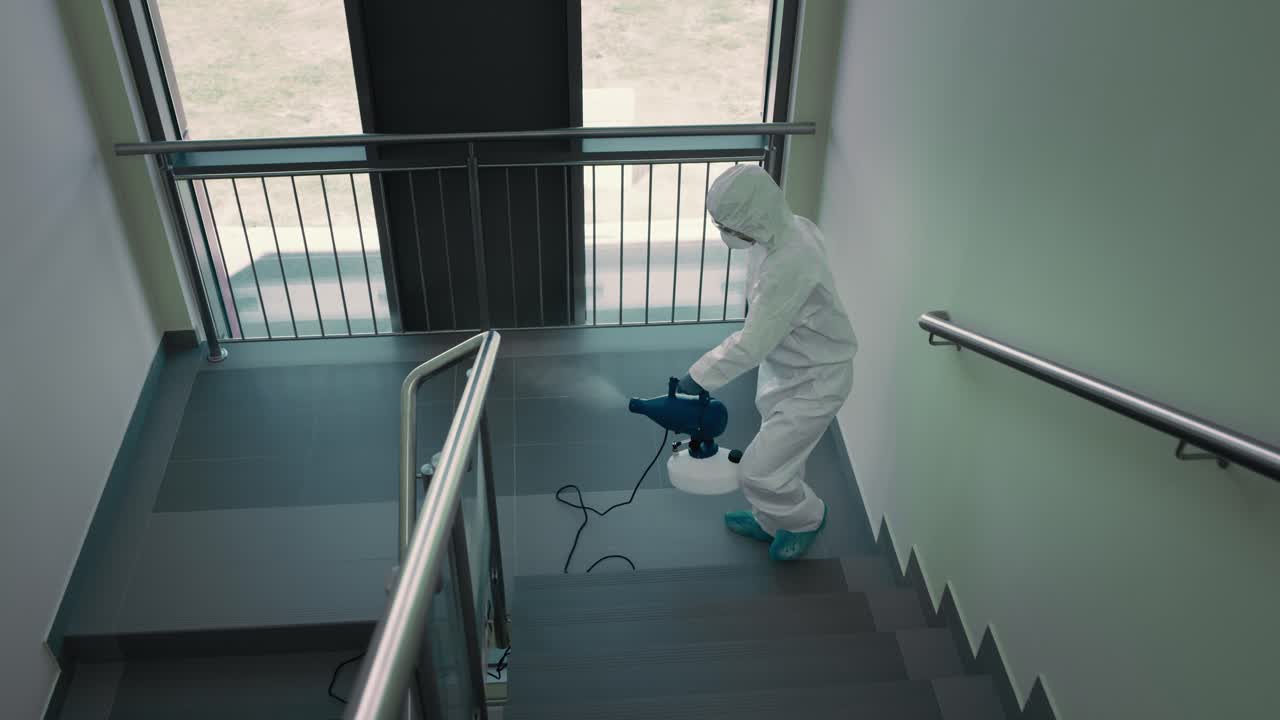 vista desde arriba de una persona con traje de protección desinfectando la escalera