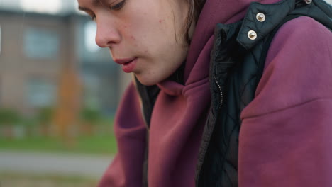 Medium shot of fitness advocate resting on metal bar after intense outdoor workout, wearing maroon sweatshirt, breathing heavily with visible effort, muscular arms on bar, blurred building background