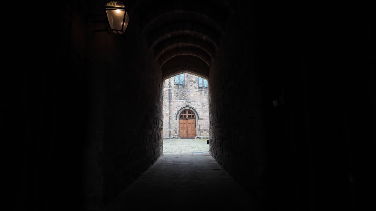 Dark castle archway creating a path to an ancient building and bright courtyard.POV