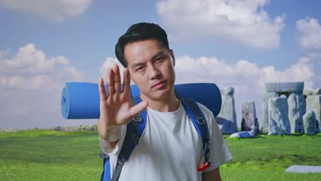close up of asian male hiker with mountaineering backpack looking at camera and making stop hand sign while traveling in stonehenge