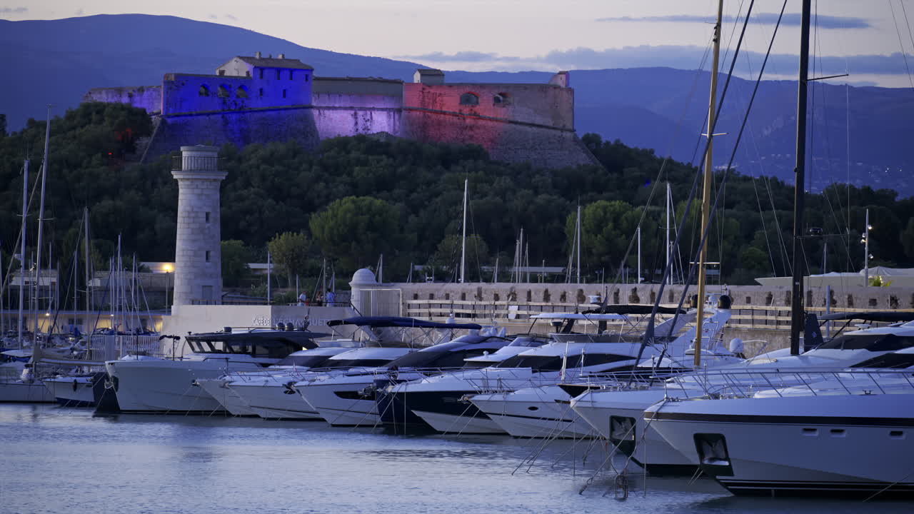 Antibes, France - June 8, 2025: Boats docked in Port Vauban with Fort Carre illuminated on the background in the evening