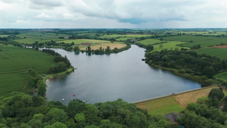 Rotierende-Drohnenansicht-Des-Cransley-Reservoirs-Mit-Spiegelung-Des-Himmels-Im-Wasser-In-England