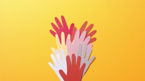 Close up of hands together made of colourful paper on yellow background with copy space