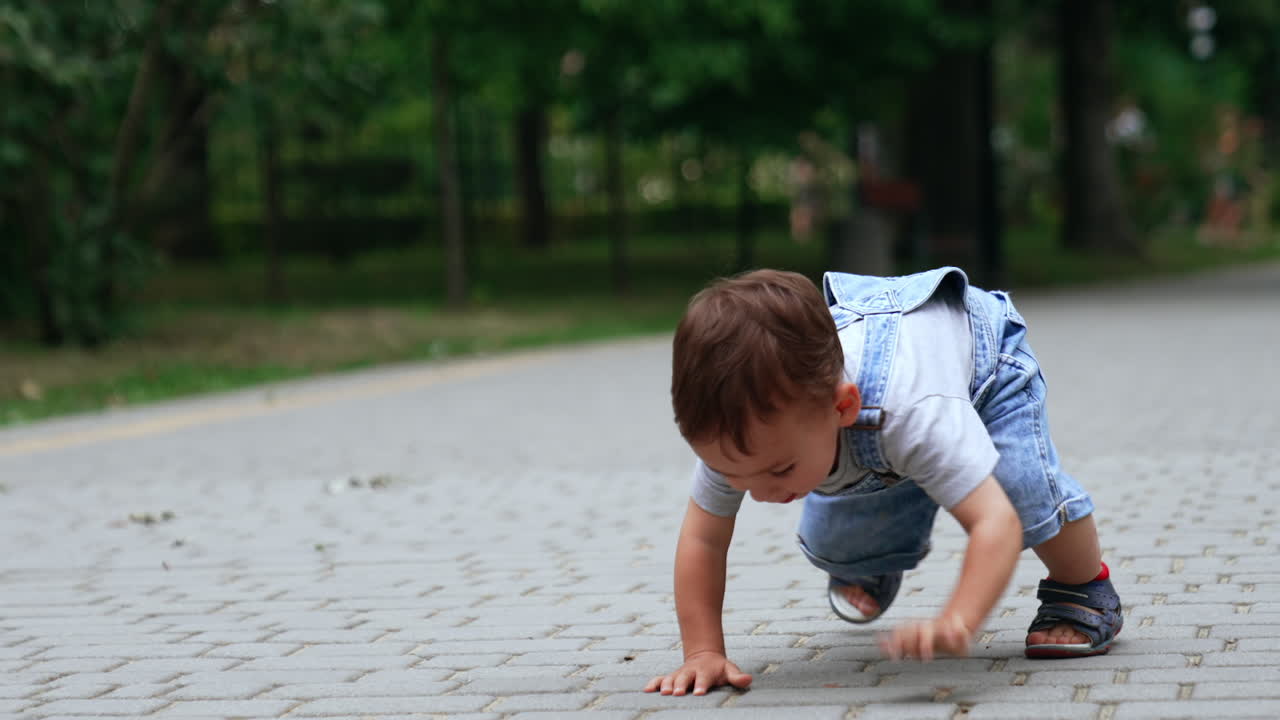 Lovely Caucasian boy sit squatted on the paved road. Adorable kid touches the tiles and crawls on his hands and feet.