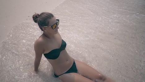 water covers young woman with hair bundle lying on beach