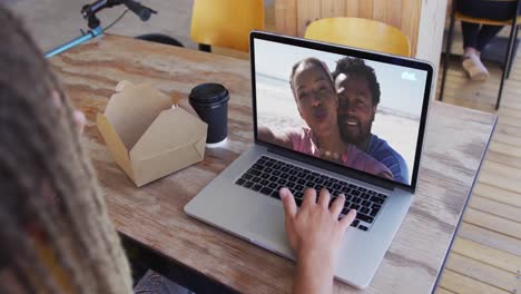 Frau-Isst-Einen-Snack,-Während-Sie-Im-Café-Einen-Videoanruf-Auf-Dem-Laptop-Führt