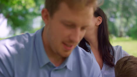 Young-couple-watching-tablet-on-nature-close-up.-Happy-family-have-fun-on-picnic