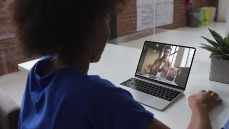 back view of african american woman having a video call with male colleague on laptop at office