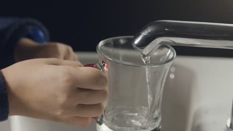 close-up image of hands trying to fill water from tap to glass