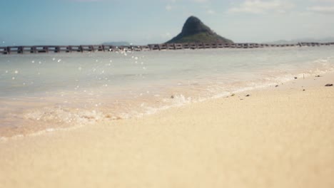 Primer-Plano-De-Una-Pequeña-Ola-Rompiendo-En-Una-Playa-Contra-La-Arena-Con-Sombrero-Chino-Mokoli&#39;i-Al-Fondo-En-Oahu,-Hawaii