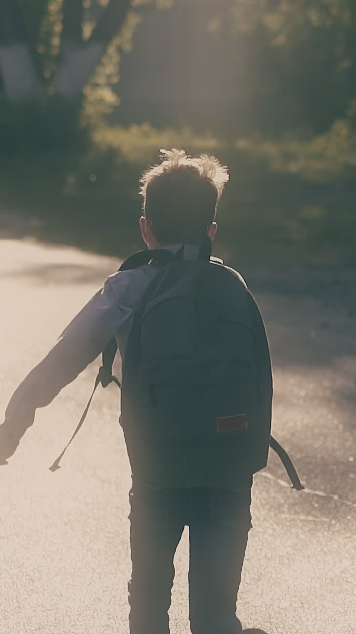 young guy with schoolbag jumps on grey asphalt road and throws up sheets when skips school slow motion backside view