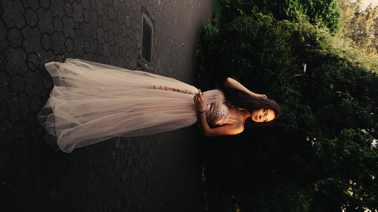 긴 분홍색 웨딩 드레스를 입은 아름다운 젊은 갈색 여성, 신부, 기다리고, 포즈, 머리카락과 함께 놀고, 기분이 좋지 않은 조명, 일몰, 숲 배경, 영화 느린 동작, 수직