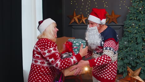 grandfather santa claus gifting christmas present box to surprised grandmother senior couple family