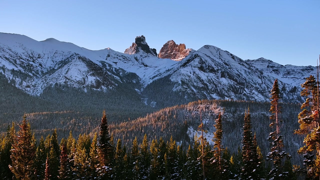 Sunrise light on snowy mountain ridge above pine forest near Cooke City Montana, aerial establishind descend