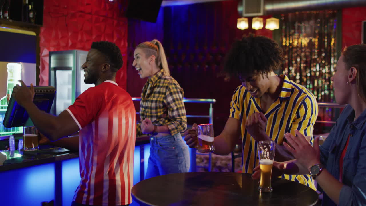 video di un gruppo diversificato di amici felici che bevono e guardano una partita sportiva in un bar, che festeggiano