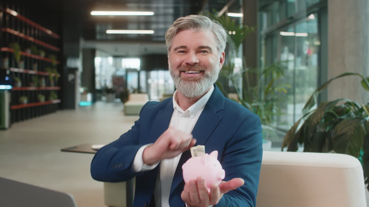 un hombre de negocios maduro y feliz ahorra dinero usando una alcancía rosa poniendo dólares en el vestíbulo de la oficina.