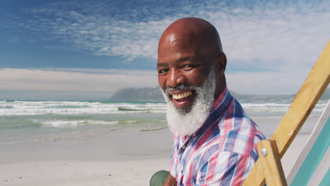 portrait of mixe race senior man sitting on subed and smiling at the beach