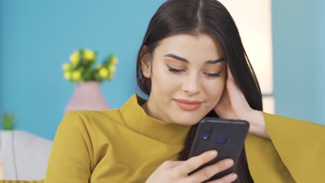 mujer feliz usando un teléfono inteligente relajándose en el sofá en casa, mirando publicaciones en las redes sociales, disfrutando de las compras en línea.