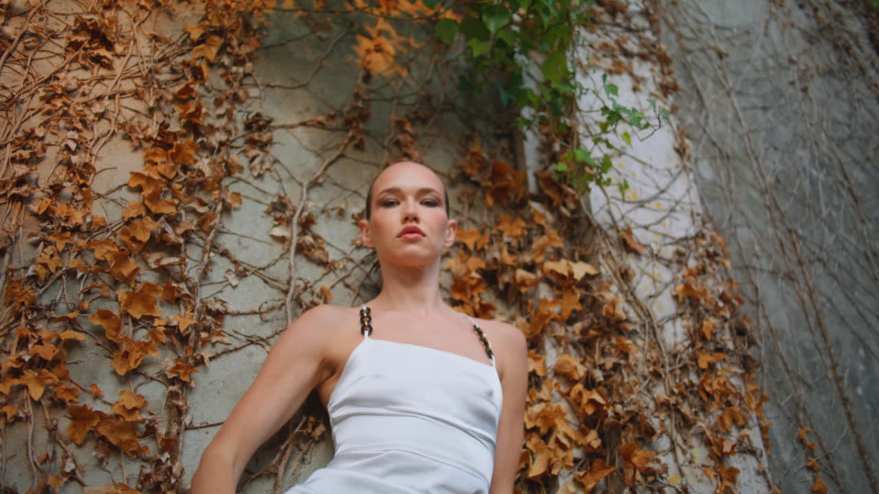 고급스러운 소녀가 오래된 벽에 기대어 자연을 포즈하고 있습니다. 화려한 모델을 찾는 카메라