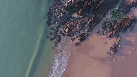 Aerial-top-view-of-sandy-coastline-with-turquoise-foaming-sea-waves-breaking-on-beach-and-rocks