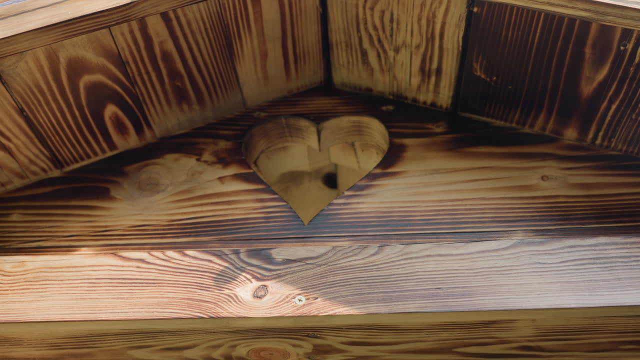 Heart shaped cutout on wooden building rooftop surrounded by rich wood grain and sunlit textures, highlighting warm rustic craftsmanship and natural patterns with screw details