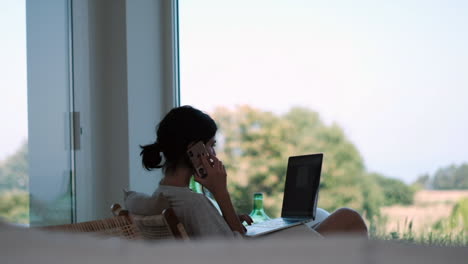 Frau,-Die-Aus-Der-Ferne-Am-Laptop-Mit-Telefon-In-Einem-Modernen-Zuhause-Arbeitet