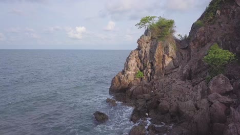 aerial: flying over a rocky hill near the ocean,with a single green tree on top of it, chantaburi province, thailand