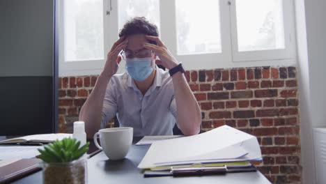 Stressed-man-wearing-face-mask-massaging-his-temples-at-office