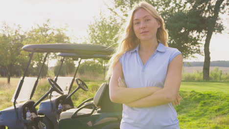 portrait of female golfer standing by buggy on golf course