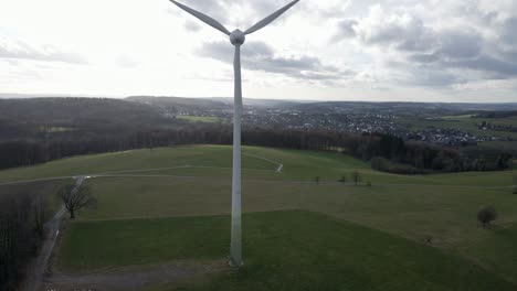 turbina eólica de giro rápido rodeada de prados verdes y parches marrones de bosque debajo de un cielo nublado